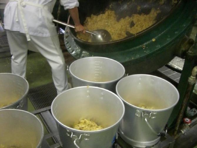 白色の作業着を着たスタッフが、5つの食缶に炊き上がったたけのこごはんを大きなおたまを使って入れている写真