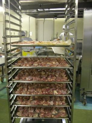 オーブンの天板の上にカットされた鶏肉が並べられ、大きなラックに積んである写真