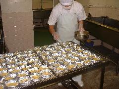 白い作業着を着たスタッフが、味をつけたさつまいもをアルミカップに盛り付けて卵黄を塗っている写真