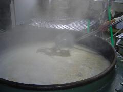 大きな釜に入れた大豆を湯がきながら大きなおたまであくをすくっている写真