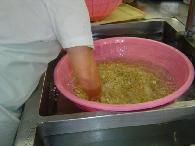 ピンク色の大きなザルに入った大豆をシンクに張った水の中に入れてスタッフが洗っている写真