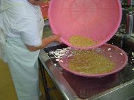 白い作業着を着たスタッフが、ピンク色の大きなザルをシンクに浸して大豆を入れている写真