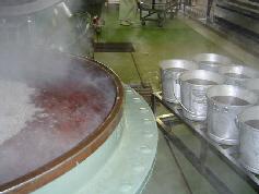 茶色の液体が入った沢山並んだ食缶と大きな釜に湯気が立って煮込んでいる写真