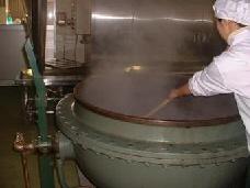 白い作業着を着たスタッフが、大きな釜で煮ている小豆をゆっくりかき回している写真