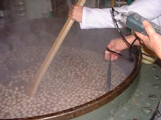 大きな釜で煮ている小豆に白玉もちを投入してかき回し、温度を計っている写真
