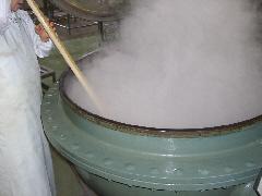 白い作業着を着たスタッフが、湯気が出ている大きな釜の中をかき混ぜている写真