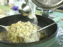 大きな釜で混ぜ合わせた材料に大量の小麦粉を振り入れている写真