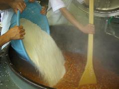 大きな釜で煮たスープに大量のお米を入れ木べらで混ぜている写真