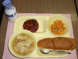 給食トレーの上に、ワンタンスープ、れんこんハンバーグ、キャロットサラダ、バターロールパン、左上に牛乳瓶が置いてある写真