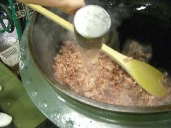 大きな釜で鶏肉を炒めているのを、大きな木べらでかき混ぜている写真