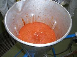 トマト缶やりんごなどの材料をアルミで作られたミキサーにかけている写真