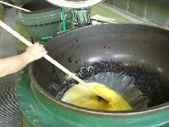 大きな釜に入れた大量のバターを熱で溶かしてかき混ぜている写真