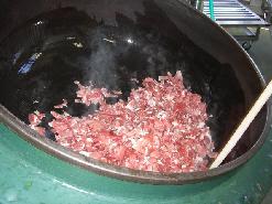 大きな釜を手前に傾けて、カレーの材料の肉を炒めている写真