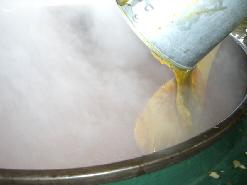 湯気が出ている大きな釜の中に、食缶に入れた完成したカレールーを入れている写真