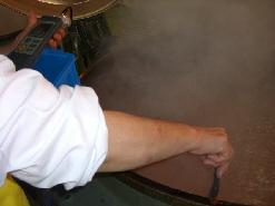 白色の作業着を着たスタッフが、大きな釜で煮込んだカレーの中に温度計を入れて温度を計っている写真